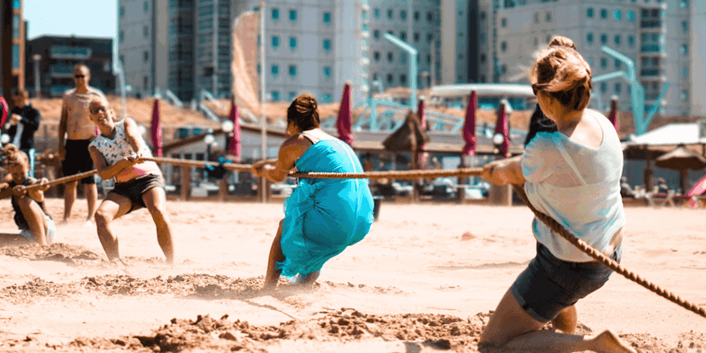 Bedrijfsuitje Expeditie Robinson Scheveningen op het strand, waar collega’s samenwerken en strijden in uitdagende teambuilding spellen.